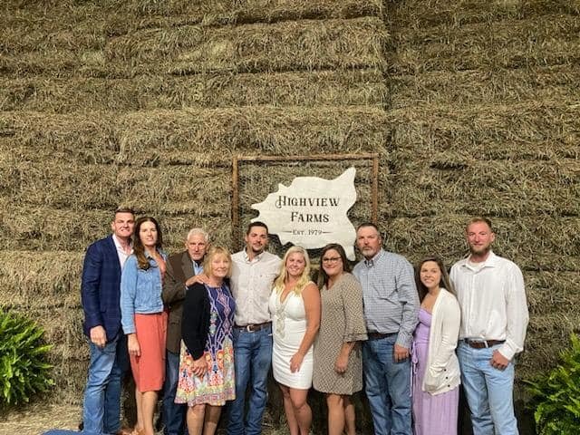 Group of people posing in front of the Highview Farms sign, established in 1979, with a backdrop of hay bales, showcasing a family or community gathering at a farm event.